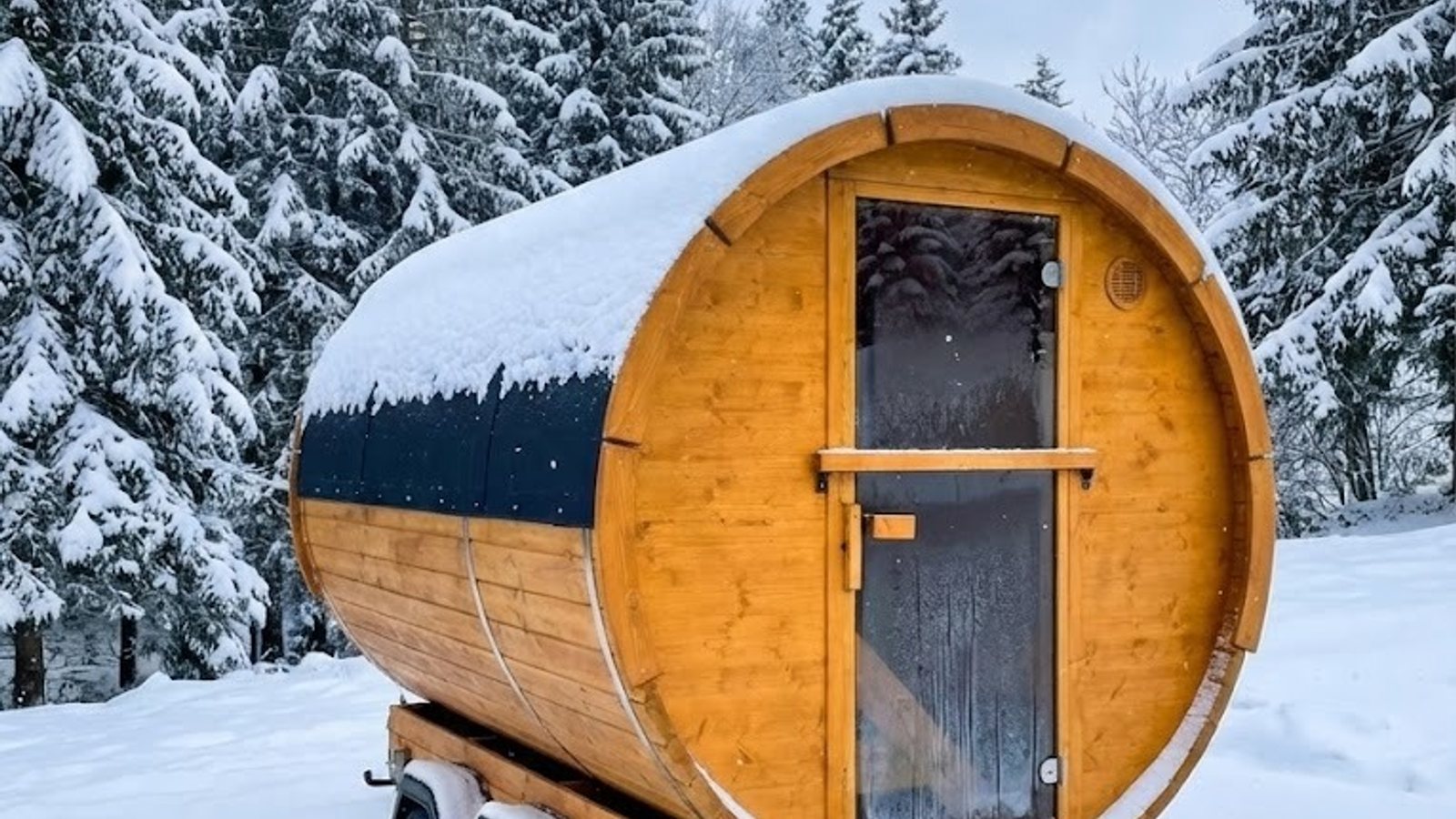 Fasssauna auf einem Anhänger im verschneiten Fichtenwald